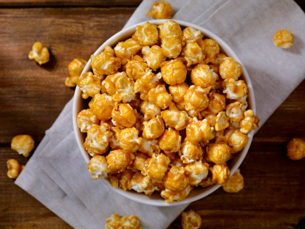 A bowl of caramel popcorn on a light-colored cloth with some popped corn scattered around.