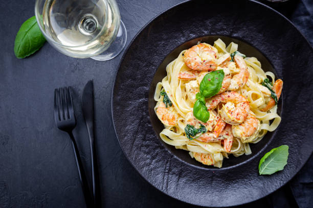 A plate of pasta with shrimp, spinach, and a garnish of basil, served with a glass of white wine.