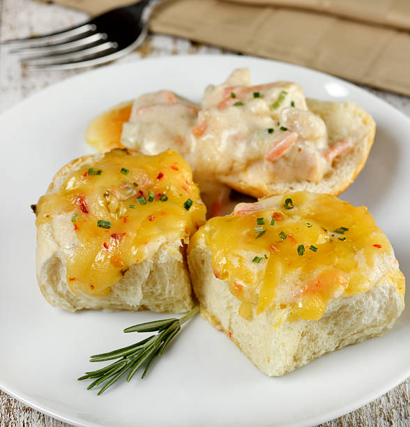 Delicious baked rolls topped with cheese and seafood sauce served on a white plate.