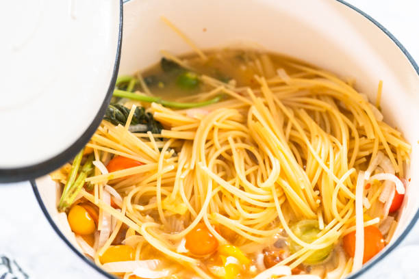 A close-up view of spaghetti noodles in a pot with colorful vegetables and broth.