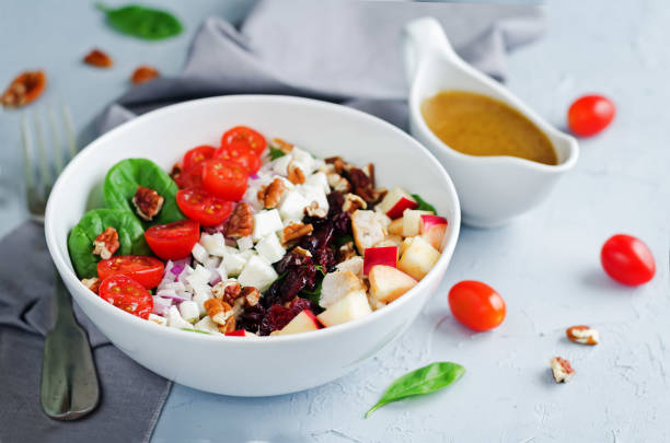 A fresh salad bowl with spinach, cherry tomatoes, chopped apples, cheese, and walnuts, accompanied by a serving of salad dressing.