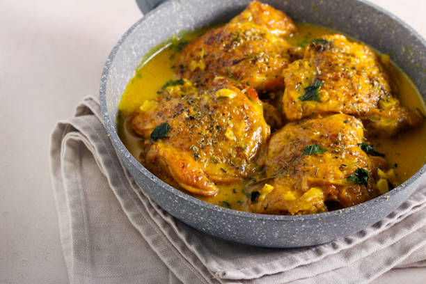 A close-up of pan-fried chicken thighs in a flavorful sauce, garnished with herbs, on a beige cloth.