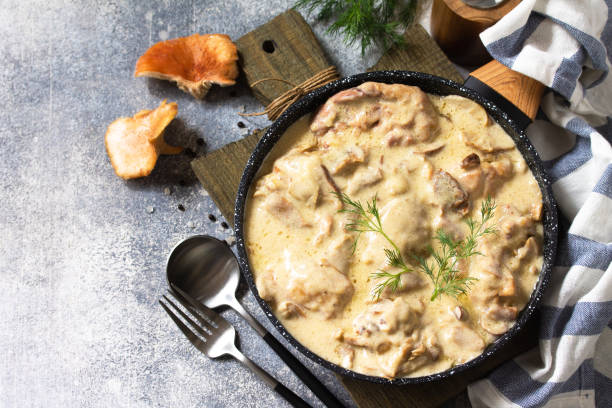 A bowl of creamy mushroom stew garnished with fresh herbs, served on a wooden board with cutlery and mushrooms around it.