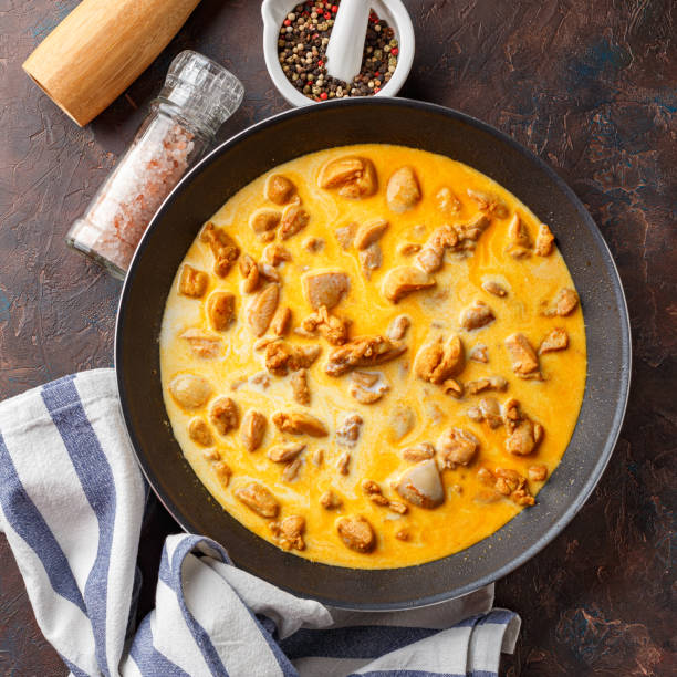 A pan filled with creamy chicken pieces in sauce, accompanied by a striped kitchen towel and condiments.