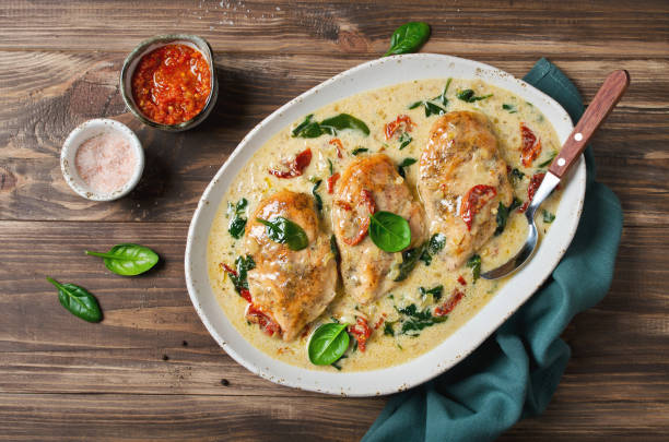 Creamy chicken dish with sun-dried tomatoes and fresh spinach served in a white dish on a wooden table.