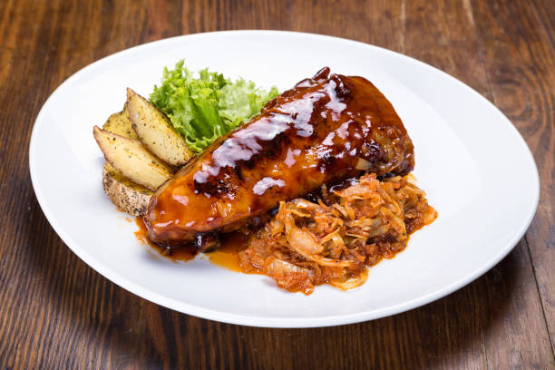 A plate of glazed chicken breast served with shredded cabbage, potato wedges, and fresh lettuce leaves.