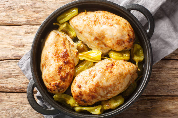 Three golden-brown chicken breasts surrounded by peppers in a black pot on a wooden surface.