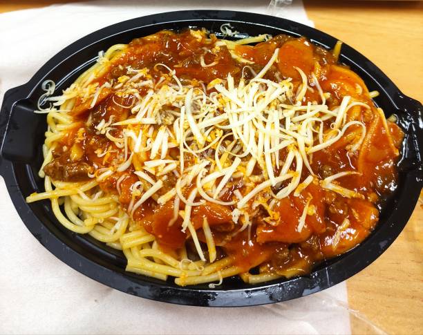 A serving of spaghetti topped with meat sauce and shredded cheese in a black takeout container.