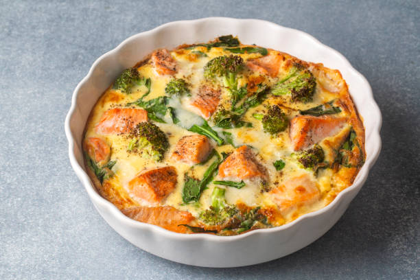 A delicious baked dish featuring salmon, broccoli, and leafy greens in a round white casserole dish.