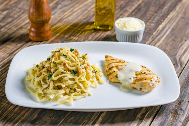 Grilled chicken breast served with fettuccine pasta and a creamy sauce on a white plate