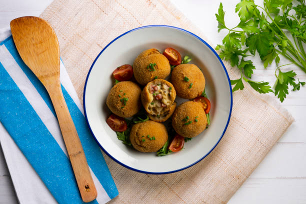 A bowl of crispy fried balls served with sliced tomatoes and greens on a light textured background