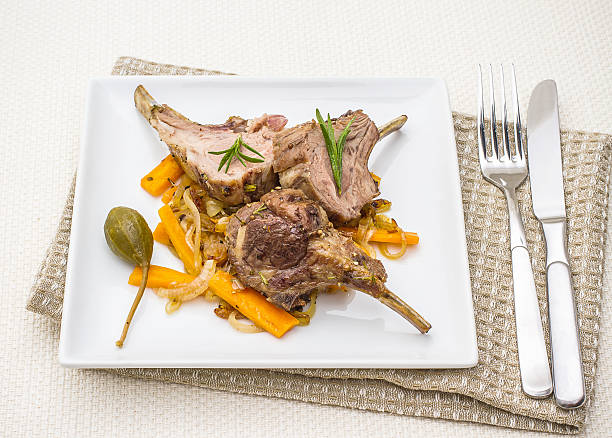 Plate of grilled lamb chops served with vegetables and garnished with rosemary.