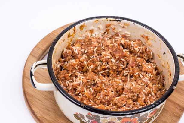 A pot filled with a hearty rice and meat dish on a wooden cutting board.