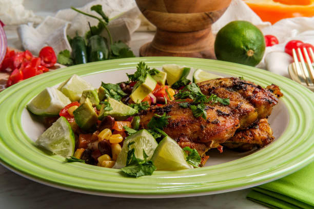 Grilled chicken served on a green plate with lime wedges and a fresh bean salad.