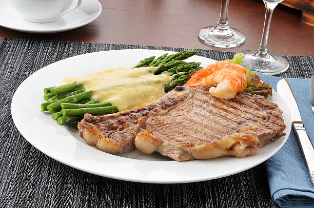 A delicious plated meal featuring grilled steak, asparagus, shrimp, and a creamy sauce.