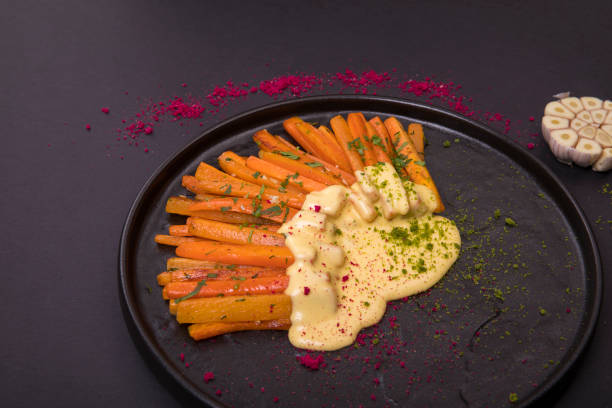 A plate of beautifully arranged carrots drizzled with a creamy sauce and garnished with herbs on a dark background