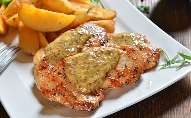 Grilled chicken breast topped with mustard sauce served alongside potato wedges.