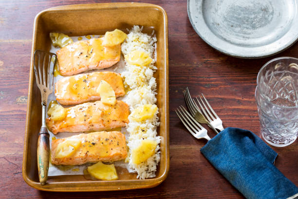 Baked salmon fillets with pineapple sauce served over rice in a brown baking dish.