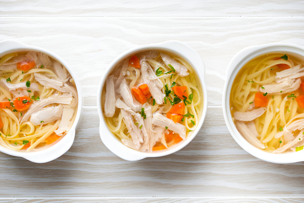 Three bowls of chicken noodle soup with vegetables and herbs.