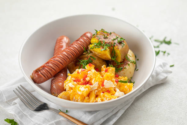 A bowl of scrambled eggs, sausages, and roasted potatoes garnished with herbs.