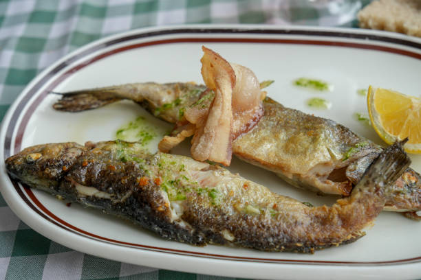 Three grilled fish garnished with bacon and lemon on a white plate with a red border