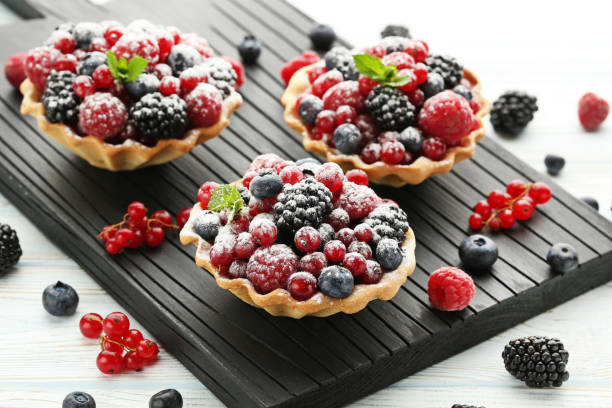 Three berry tarts on a black serving board, garnished with powdered sugar and mint.