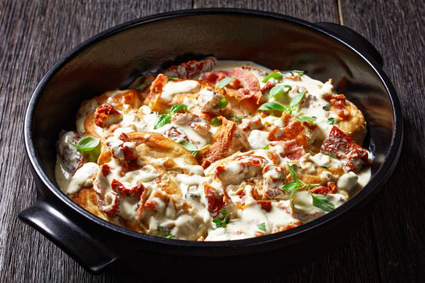 A creamy dish with bacon and sun-dried tomatoes served in a black bowl on a wooden table.