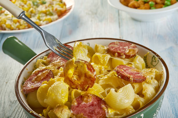 A close-up of a dish of creamy pasta with slices of sausage being lifted by a fork, placed in a decorative bowl.