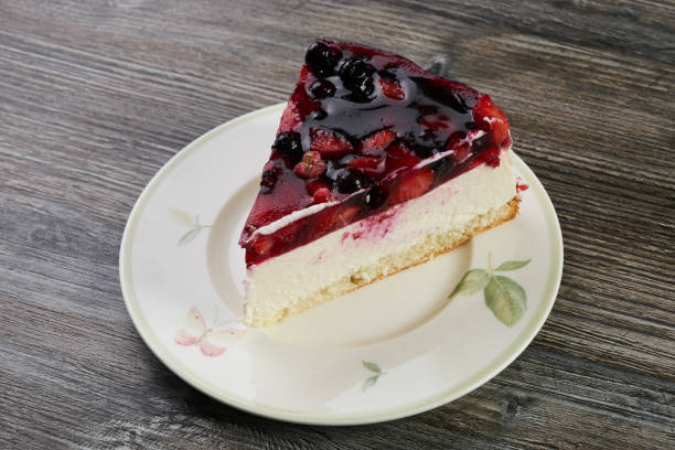 A slice of berry cheesecake topped with mixed berries and jelly on a decorative plate.