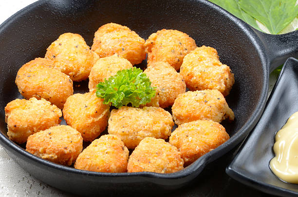 A skillet filled with golden-brown fried cheesy bites garnished with a sprig of parsley and accompanied by a small dish of mustard.