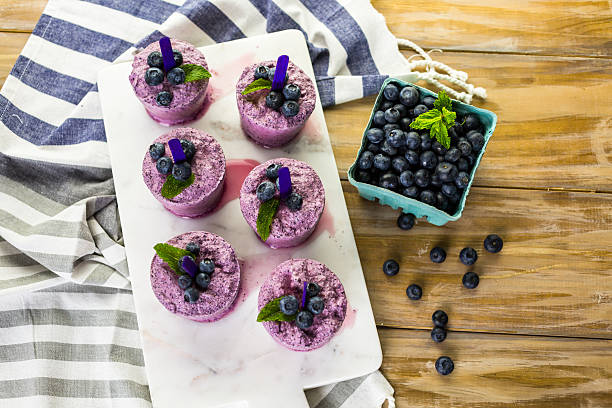 A display of colorful blueberry popsicles garnished with mint leaves, placed on a marble tray with a container of fresh blueberries nearby.