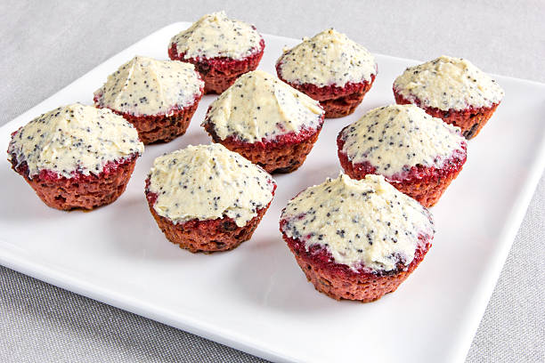 A platter of red velvet mini cupcakes topped with a light cream frosting sprinkled with poppy seeds.