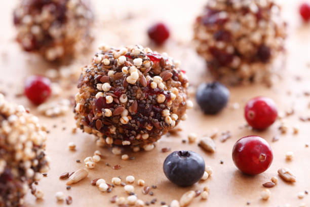 Healthy energy balls coated with seeds and surrounded by berries on a parchment surface.