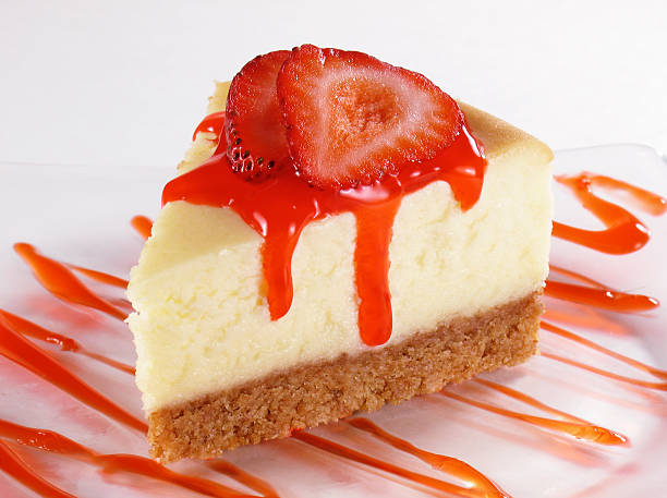 A slice of cheesecake topped with fresh strawberries and a drizzle of red sauce on a plate.