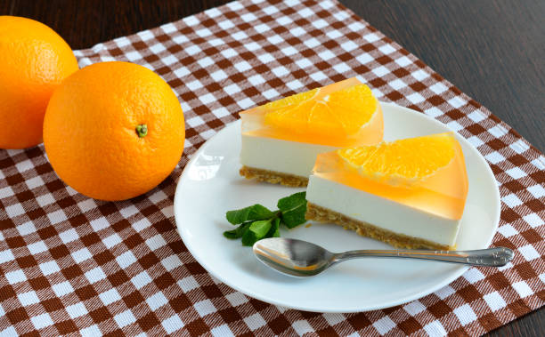 A plate of orange-flavored cheesecake slices with fresh oranges and a mint garnish on a checkered tablecloth.