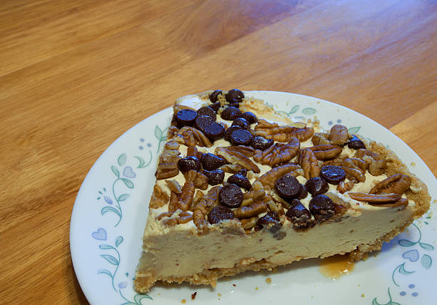 A slice of cheesecake topped with chocolate chips and pecans on a decorative plate.