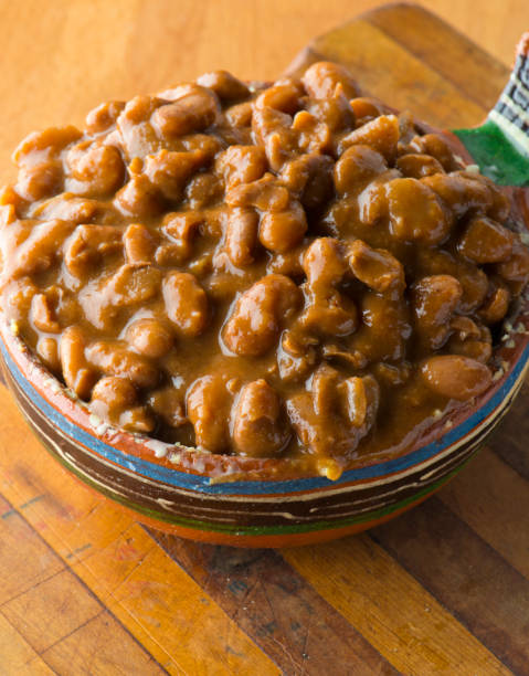 A close-up of a ceramic bowl filled with hearty brown beans in a rich sauce, placed on a wooden cutting board.