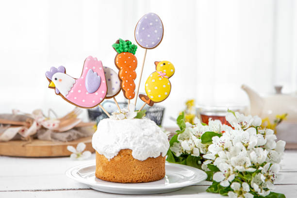 A decorative Easter cake topped with colorful icing and themed cookies including a chicken, an egg, and a carrot, surrounded by flowers.