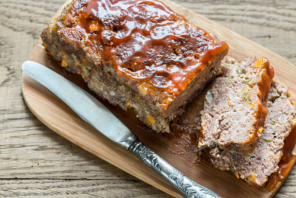 A meatloaf served on a wooden cutting board with a knife beside it, sliced to show the inside.