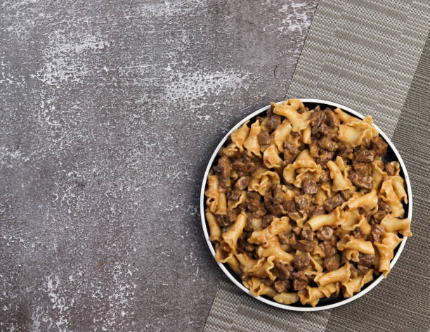 A bowl of beef and noodle dish on a textured tabletop.