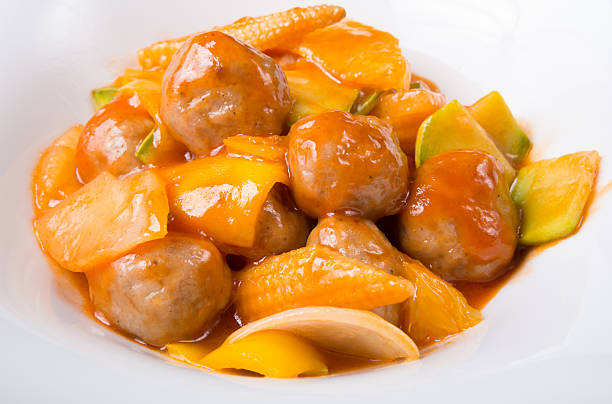 A close-up of a dish featuring meatballs in a sweet and sour sauce with vegetables.