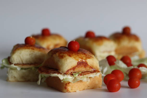 Mini sandwich sliders topped with cherry tomatoes on a white background.