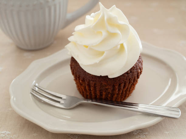 Chocolate cupcake topped with frosting on a plate with a fork