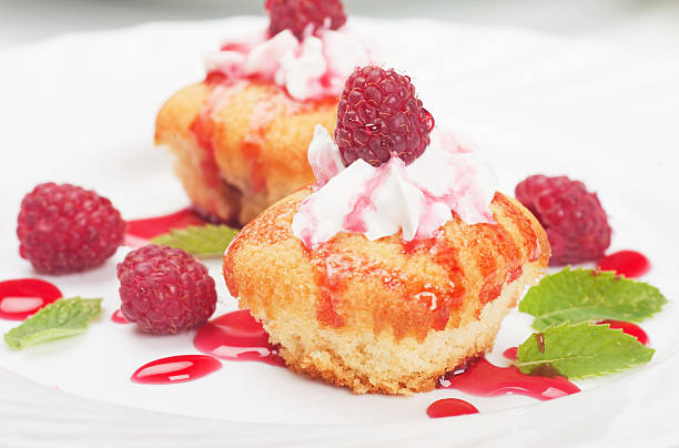 Delicious raspberry cupcakes topped with whipped cream and raspberry sauce, garnished with fresh raspberries and mint leaves.