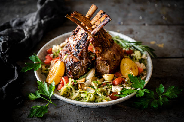 A delicious plate of grilled lamb chops atop a bed of fresh salad with tomatoes, zucchini, and garnished with parsley and lemon.