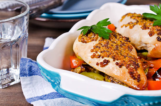 Baked chicken breasts topped with mustard and served with mixed vegetables in a blue dish on a wooden table.