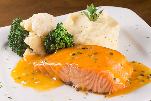 A plate of salmon fillet with passionfruit sauce, served with steamed broccoli, cauliflower, and mashed potatoes.