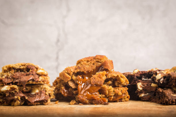 Close-up of three different types of cookies with melted chocolate and caramel filling on a wooden surface.