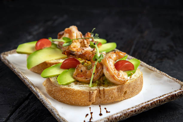 Gourmet avocado toast topped with grilled shrimp and cherry tomatoes on a decorative plate