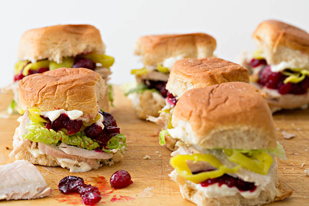 Assorted mini sandwiches with turkey, cranberry sauce, pickles, and lettuce on a wooden cutting board.